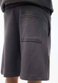 Donkergrijze katoenen shorts met een elastische tailleband, zijzakken en een patchzak aan de achterkant. Gecoate textuur met gestikte randen.