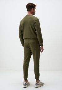 Olive green sweatshirt and joggers set. Soft fabric, tapered pants with elastic cuffs, and a back pocket detail. Casual athletic wear.