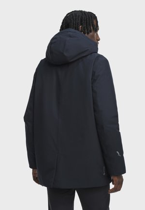 Un homme portant une veste noire à capuche en GORE-TEX, de dos, montrant le dos et le côté droit sur un fond gris clair uni.
