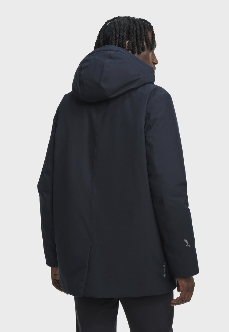 Man wearing a black hooded GORE-TEX jacket facing away, showing back and right side against a plain light gray background.