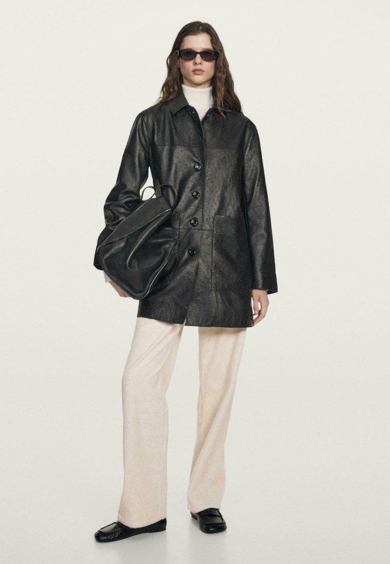 Černá umělá kožená bunda s knoflíky, předními kapsami, vrstvená přes světlejší rolák. V doplnění s bledými kalhotami a černou taškou, elegantní design.