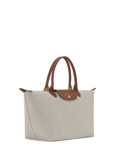 Beige rectangular handbag with brown leather handles and flap, gold button, and zipper closure, displayed on white background.