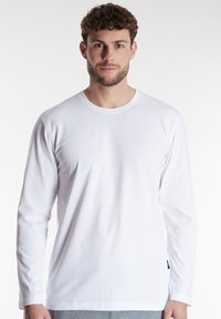 White long-sleeve t-shirt made of soft fabric with a crew neckline and relaxed fit. Displays minimalistic design, no patterns or embellishments.