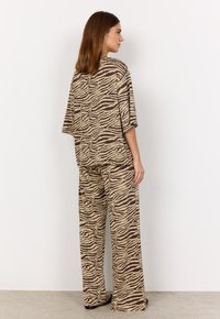 Übergroßes beiges Outfit mit braunem Zebra-Muster; beinhaltet ein locker sitzendes Oberteil und weite Hosen, hergestellt aus weichem Stoff mit glatter Textur.