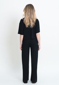 Top corto nero con maniche corte abbinato a pantaloni neri larghi. Tessuto morbido con una vestibilità rilassata. Modello visto da dietro.