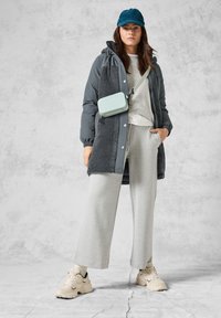 Manteau gris matelassé avec des accents en polaire, sweat-shirt gris clair et pantalon large, sac bandoulière menthe, casquette bleue et baskets beiges.