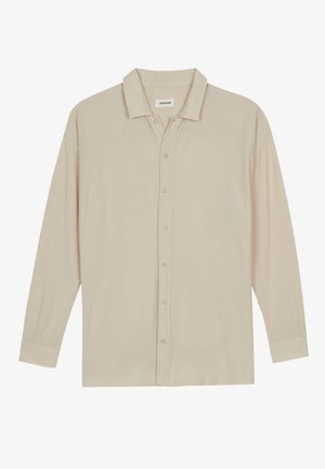 Chemise beige à manches longues en ribbed, avec un col et des boutons sur le devant, posée à plat sur un fond blanc.