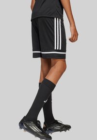 Schwarze Sportshorts mit weißen Streifen, passende schwarze Socken und schwarze Fußballschuhe, die ein Schnürdesign und geformte Stollen für besseren Halt bieten.
