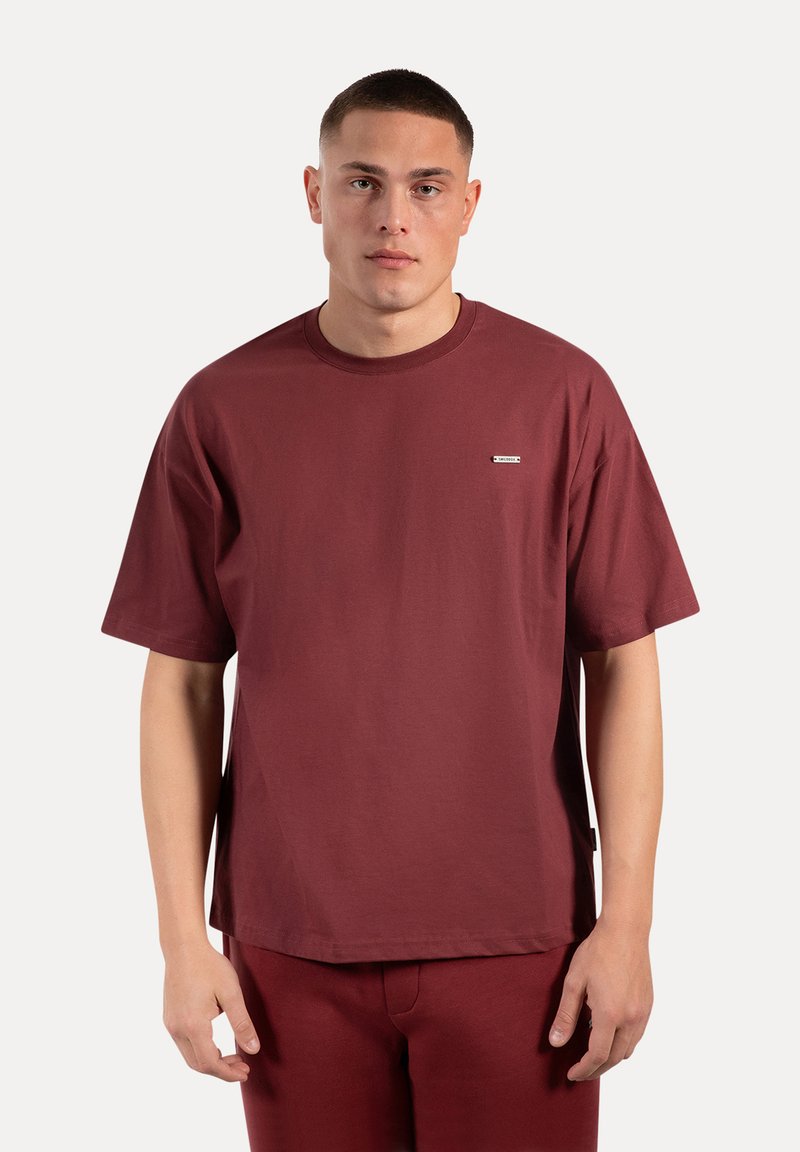 Maroon katoenen t-shirt met een ronde hals, korte mouwen en een klein merklabel op de linkerborst, ontworpen met een ontspannen pasvorm.