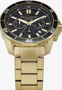 Kuldne metallkell musta tekstuuriga dials, kronograafalustega ja julgete tundemarkeritega. Omab vastupidavat kuldset käevõru ja 100 meetri veekindlust.