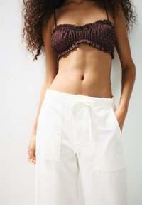 Hnedý crop top s bodkami a volánmi, skombinovaný s voľnými bielymi bavlnenými nohavicami so sťahovacím pásom a bočnými vreckami.