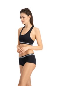 Zwarte sportbeha en bijpassende boxershort, met een logo tailleband en een naadloos ontwerp. De stof lijkt zacht en rekbaar.