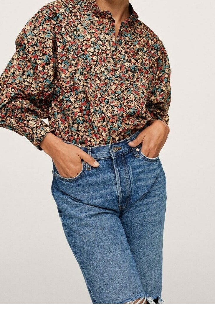 Personne portant un chemisier floral à manches longues rentré dans un jean en denim bleu taille haute, les mains dans les poches avant.