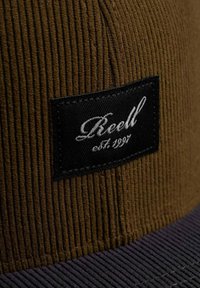 Brown corduroy cap with a black fabric patch featuring white embroidered text. Cap has a textured surface and a flat brim.