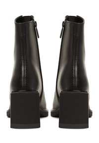 Botas de cuero negras hasta el tobillo con tacón cuadrado, cierre de cremallera, textura suave y diseño sencillo. Construcción robusta con detalles cosidos.