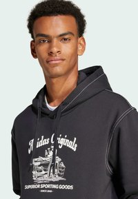 Zwarte hoodie met koord, met een witte grafische printtekst en afbeelding. Het heeft contrasterende stiksels en een ontspannen pasvorm.