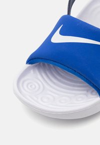 Sininen kuminen liukuva sandaali, jossa on teksturoidulta valkoiselta pohjalta ja strapissa on näkyvä valkoinen Nike-logo.