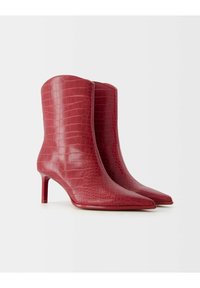 Red ankle boots made of glossy crocodile-embossed leather, featuring a pointed toe and a thin, cylindrical heel. Smooth texture, modern design.