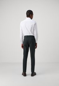 White long-sleeve shirt with a folded collar, paired with dark green tailored trousers and brown shoes, viewed from the back.