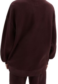Sudadera sobre tamaño en color burdeos, con puños y dobladillo acanalados, fabricada con material suave. Cuenta con una etiqueta cuadrada en la parte posterior del cuello y un corte relajado.