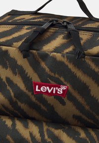 Borsa a strisce tigre nera e marrone, realizzata in tessuto testurizzato, con chiusura a zip e logo Levi's ricamato in rosso sul davanti.