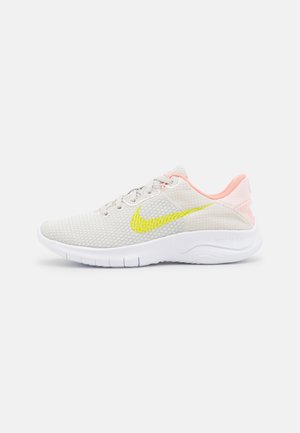 Zapatilla de running de malla gris clara con interior melocotón, logo amarillo de Nike, suela blanca flexible y diseño de tobillo bajo.