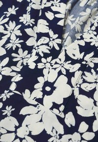 Tissu bleu foncé avec imprimé floral abstrait blanc, montrant une couture détaillée et un pli du matériau.