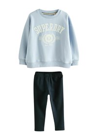 Ljusblå sweatshirt med "SUPERDRY"-logotyp i vitt, kombinerad med svarta leggings. Mjukt tyg, lös passform, ribbad mudd och midja.