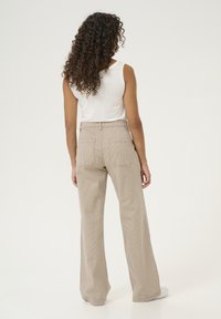 Beige, wide-leg corduroy trousers with vertical stripes, featuring dual back pockets and a fitted waist. Paired with a plain white tank top.