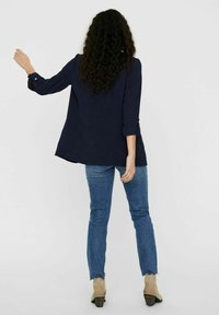Tmavě modrá bunda s dlouhým rukávem a ohrnutými manžetami, volný střih, v kombinaci se světle modrými skinny džínami a béžovými kotníkovými botami. Minimalistický styl.