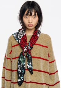 Bufanda de seda multicolor con patrones de leopardo y serpiente, predominantemente en rojo y negro, atada con estilo alrededor del cuello.