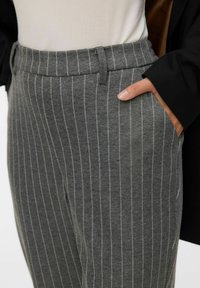 Szare w paski spodnie wykonane z miękkiego materiału, z dopasowanym stanem, szlufkami na pasek i bocznymi kieszeniami. Paski mają jaśniejszy szary kolor.