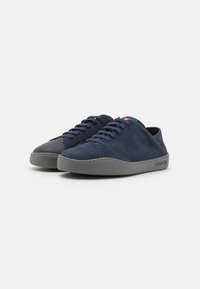Sneaker in suede navy con suola in gomma grigia, punta tonda e design con lacci. Presenta un cappuccio anteriore grigio a contrasto e una grafica minimale sul lato.