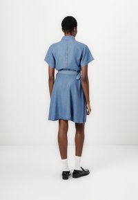 Denim shirt dress with short sleeves, a collar, and a tied waist. Features a flared skirt and raw hem. Color: medium blue.