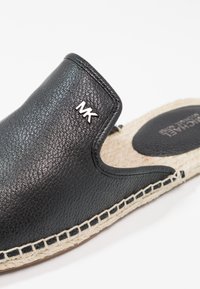Espadrille noire en cuir slip-on avec logo MK sur la tige et semelle en jute tissée, présentant des détails cousus et une semelle intérieure marquée.