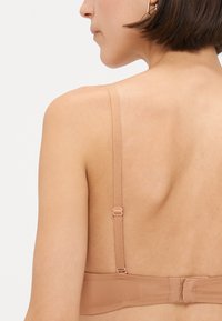 Nude podprsenka s nastavitelnými ramínky, hladkým povrchem a zapínáním na háček a ok. Bezešvý design snižuje viditelnost pod oblečením.