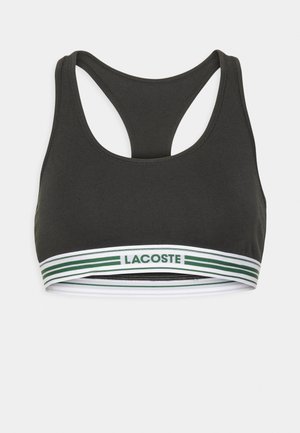 Svart sportsbh med racerback-design, med et hvitt og grønt stripete elastisk bånd med "LACOSTE"-logo. Glatt, stretchy stoff.