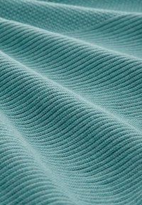 Gros plan sur un tissu doux de couleur sarcelle avec un motif tricoté côtelé horizontal texturé et de légers plis créant des ondulations ombragées.