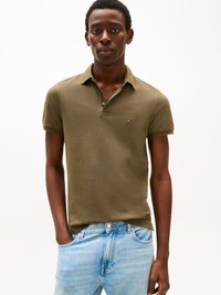 Oliivroheline polo särk, millel on kaelus, lühikesed varrukad ja diskreetne logo rinnal, koos helesiniste denim teksadega.