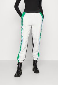 Vita träningsbyxor med gröna och blå sidopaneler, elastisk midja och muddar. Kombineras med svarta snörade kängor.