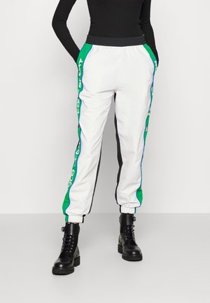 Witte trainingsbroek met groene en blauwe accenten aan de zijkant, elastische tailleband en boorden. Gecombineerd met zwarte veterlaarzen.