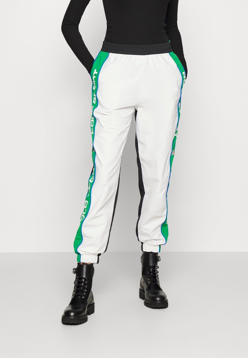 Vita träningsbyxor med gröna och blå sidopaneler, elastisk midja och muddar. Kombineras med svarta snörade kängor.