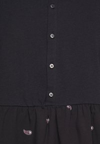 Svart knäppt klänning med en figurnära överdel och en utsvängd nedre del med små paisleymotiv. Mjuk bomullstyg med en slät struktur.