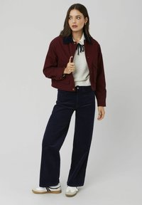 Veste courte bordeaux avec un col bleu marine, pull en tricot blanc, et pantalon large bleu marine. Baskets blanches avec des accents noirs et beiges.