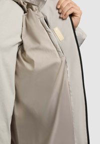 Lett, beige jakke med en glat indvendig foer, som har et mærke nær lynlåsen og et afslappet pasform design.