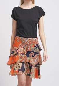 Musta lyhythihainen paita, jossa on kukkakirjailu pääntiellä, yhdistettynä oranssiin ja laivastonsiniseen, röyhelöihin koristeltuun hameeseen, jossa on paisley-kuvioita.