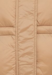 Beige jakke med dunfyll, laget av stoff med vertikale quiltepaneler, glatt tekstur og subtil glans. Sømmen er synlig i kontrastfarger.