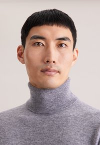 Grauer Rollkragenpullover mit gerippter Textur, hoher Halslinie und taillierter Passform. Glatter Stoff mit weichem Erscheinungsbild.