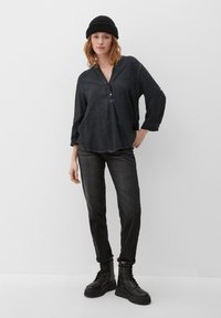 Czarna, długosleeve'owa koszula z zapinanym dekoltem, zestawiona z ciemnymi, slim-fit dżinsami i czarnymi, sznurowanymi butami wojskowymi.