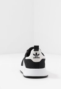 Svart atletisk sko med ovandel i mesh, vita accenter och en logotyp på hälen. Har en kontrasterande vit mellansula och en texturerad yttersula.